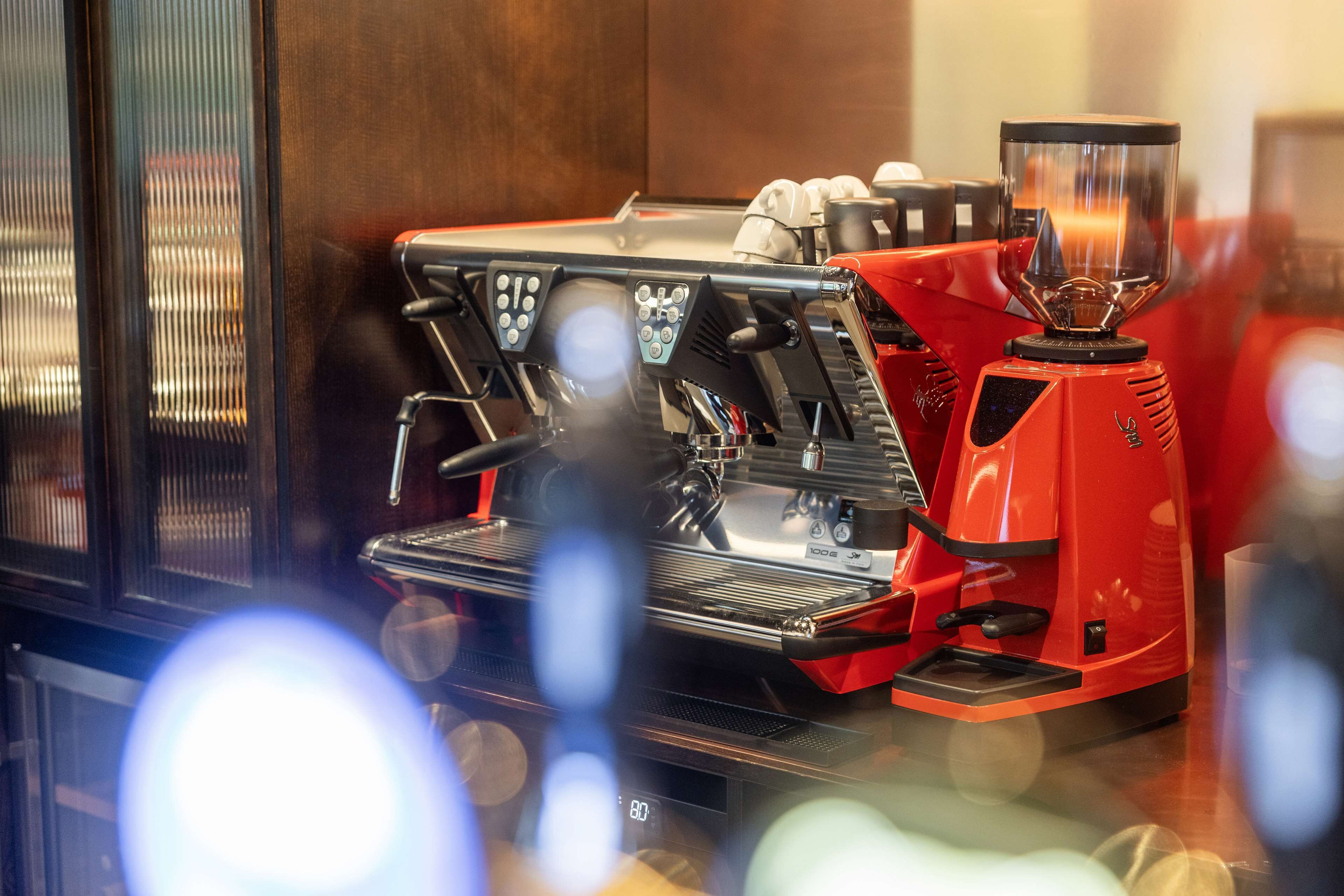Una máquina de espresso roja con pantalla digital, espumador de leche y molinillo.