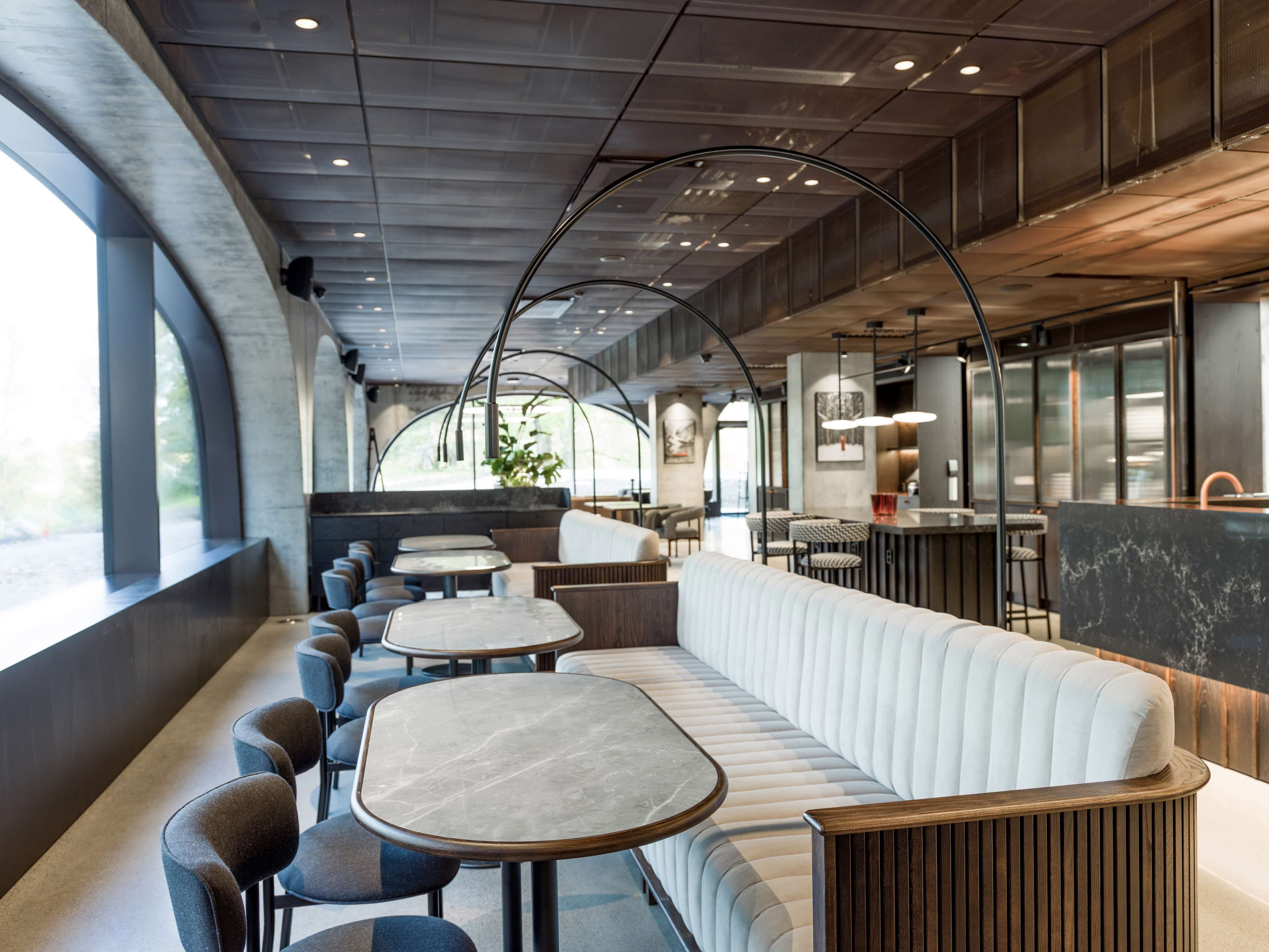 Un interior de restaurante moderno con un largo banco acolchado blanco, varias mesas redondas y una zona de bar.