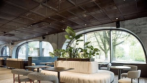 Un interior moderno con una zona de estar circular, mesas y ventanas amplias que dan vistas a árboles.