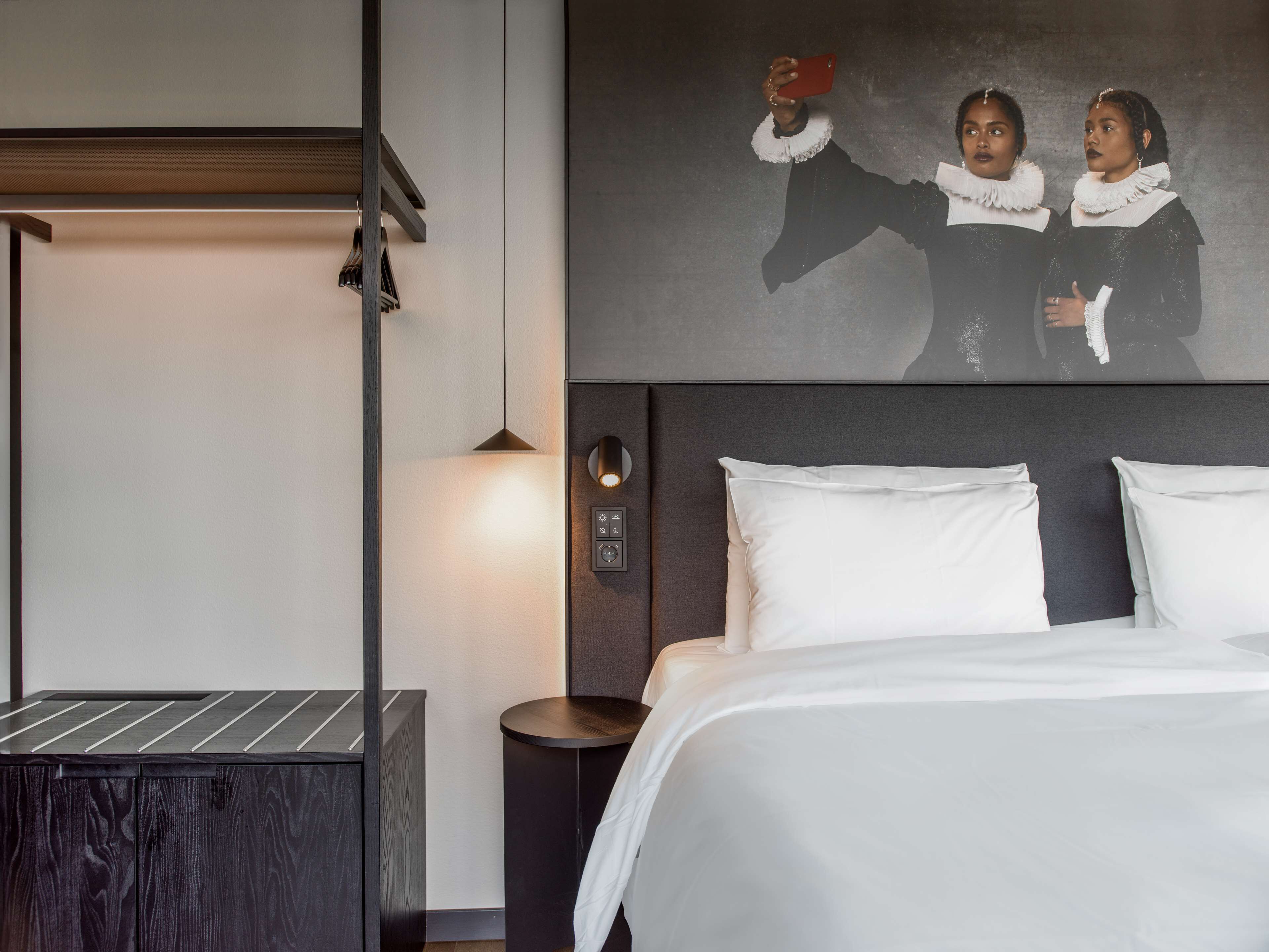 Una habitación de hotel moderna con una cama, una mesita de noche, una lámpara de pared y un panel de control.