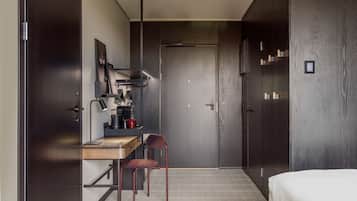 A compact hotel room with a bed, a desk with a chair, a kitchenette, and a wardrobe.