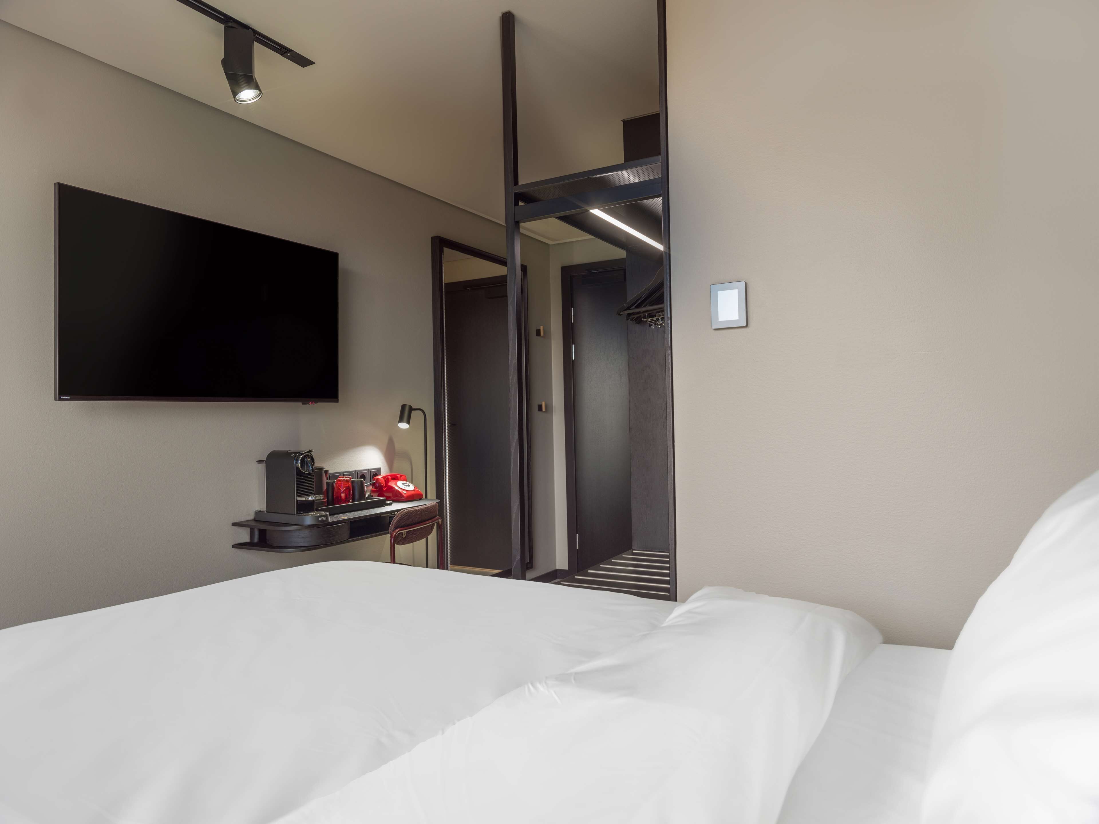 Une chambre d’hôtel moderne dotée d’un grand lit, d’un téléviseur à écran plat fixé au mur, d’un bureau avec une lampe, d’un téléphone et d’un porte-manteau.