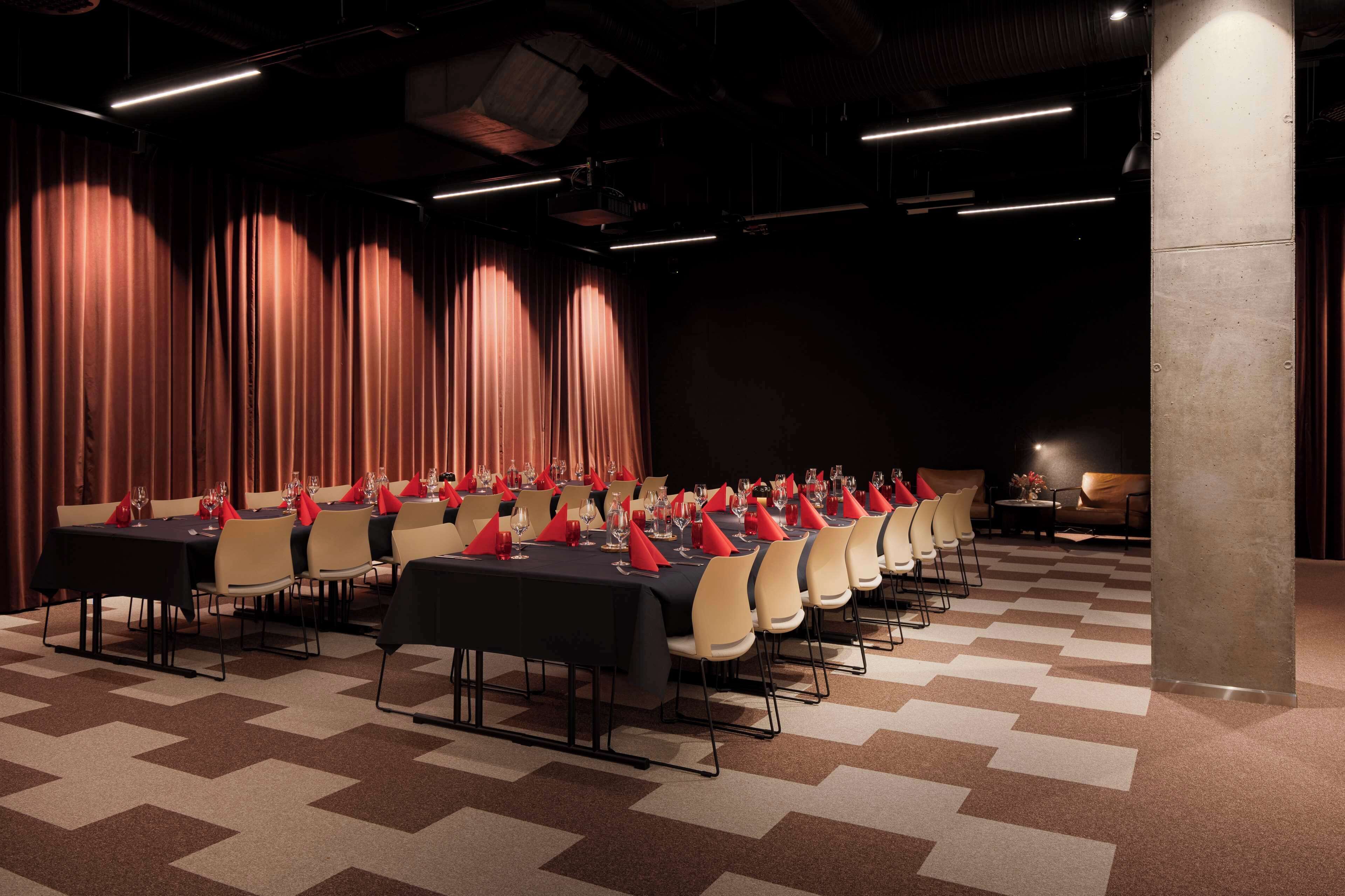 A conference room with multiple tables and chairs, arranged in rows, with a checkered carpet and curtains in the background.