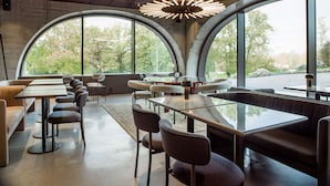Un restaurante moderno con ventanales curvos, mesas redondas y sillas.