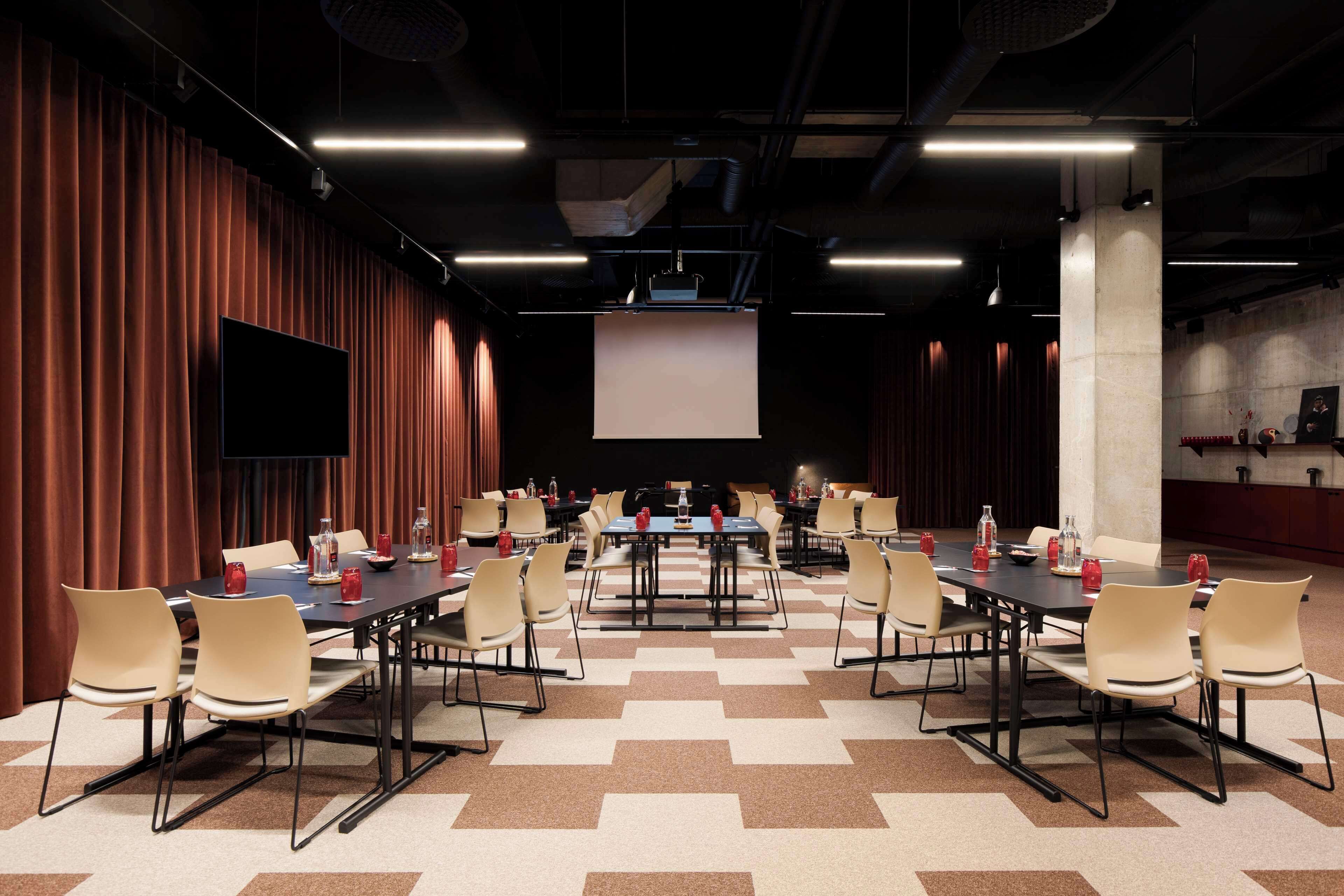 A conference room with multiple tables and chairs, a large screen, and a flat-screen TV on the wall.