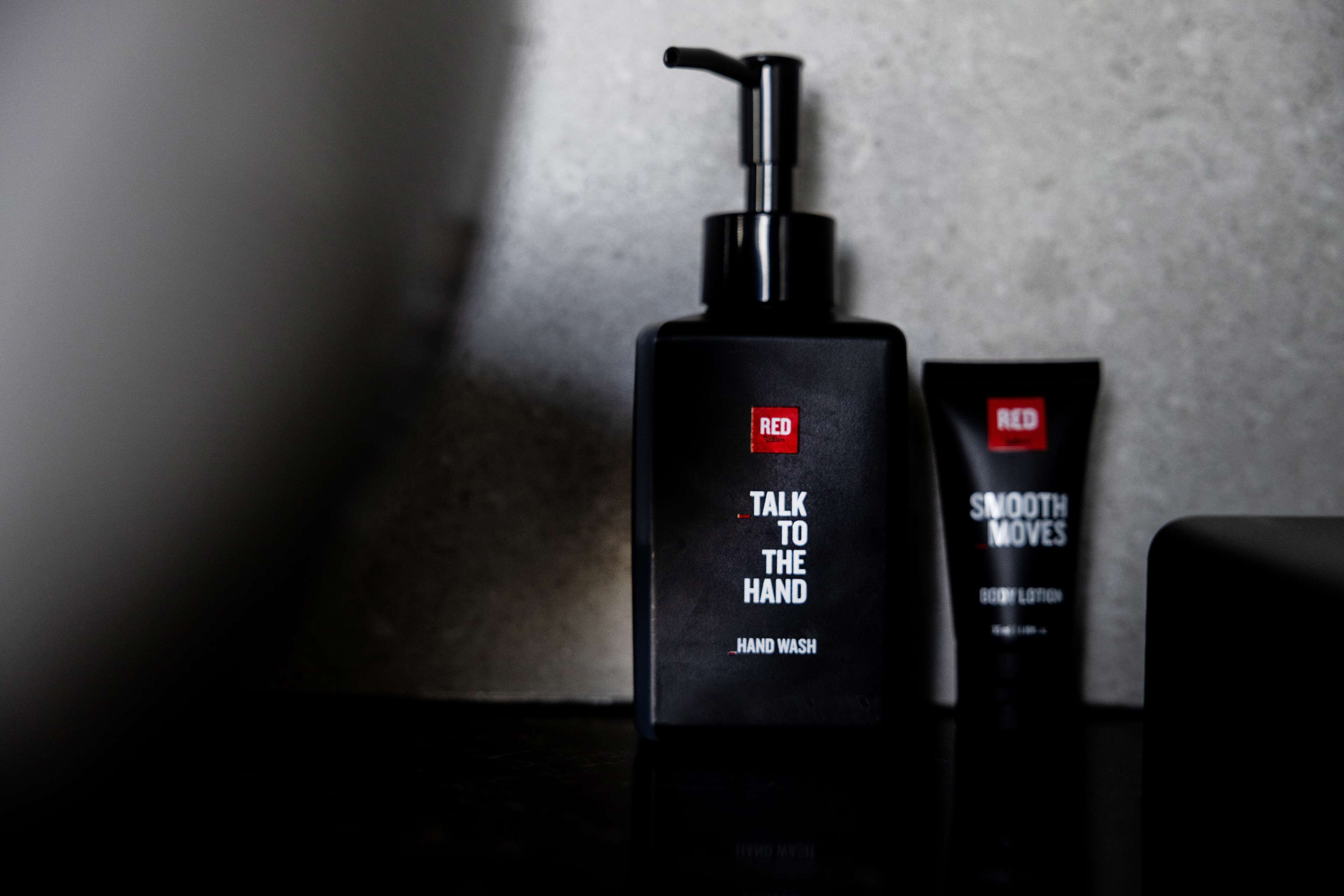 A black bottle of hand wash and a tube of body lotion with a pump dispenser, both labeled 'RED'.