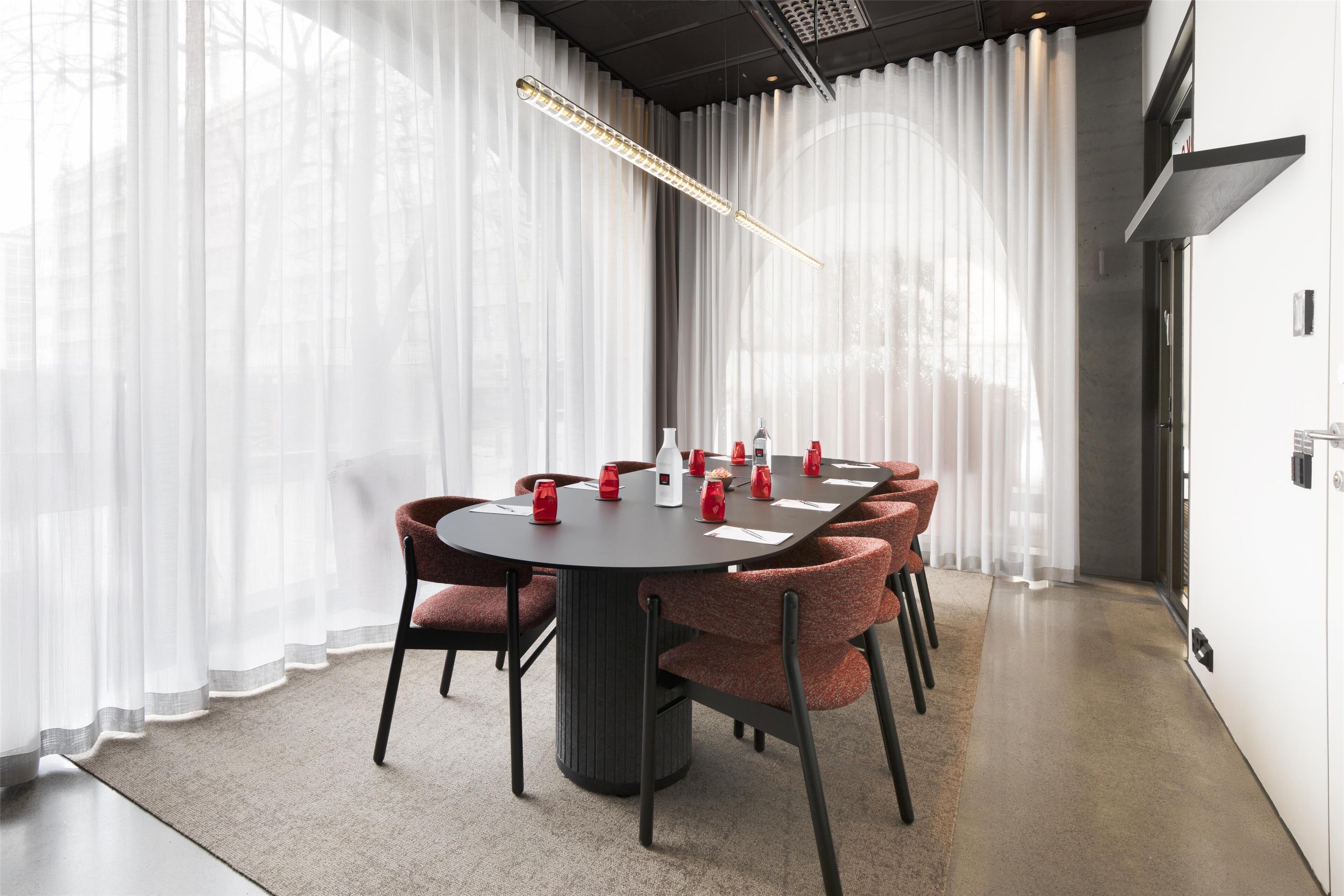 A modern conference room with a round table, red upholstered chairs, and a pendant light.