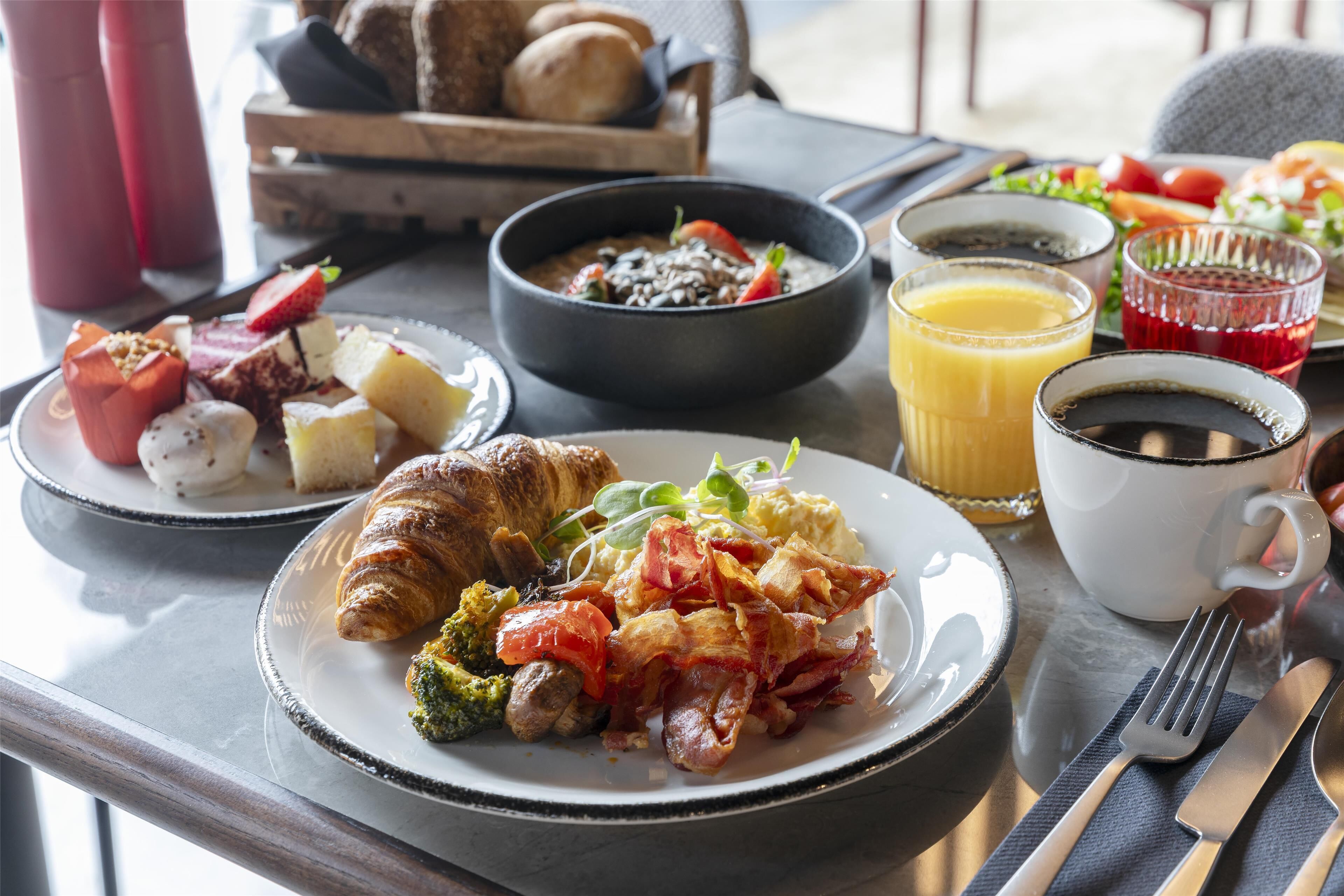 Een ontbijttafel met croissants, roerei, spek, tomaten en een fruitsalade.