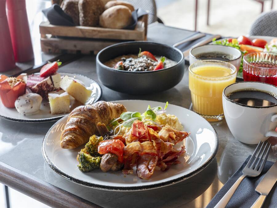 Een ontbijttafel met croissants, roerei, spek, tomaten en een fruitsalade.
