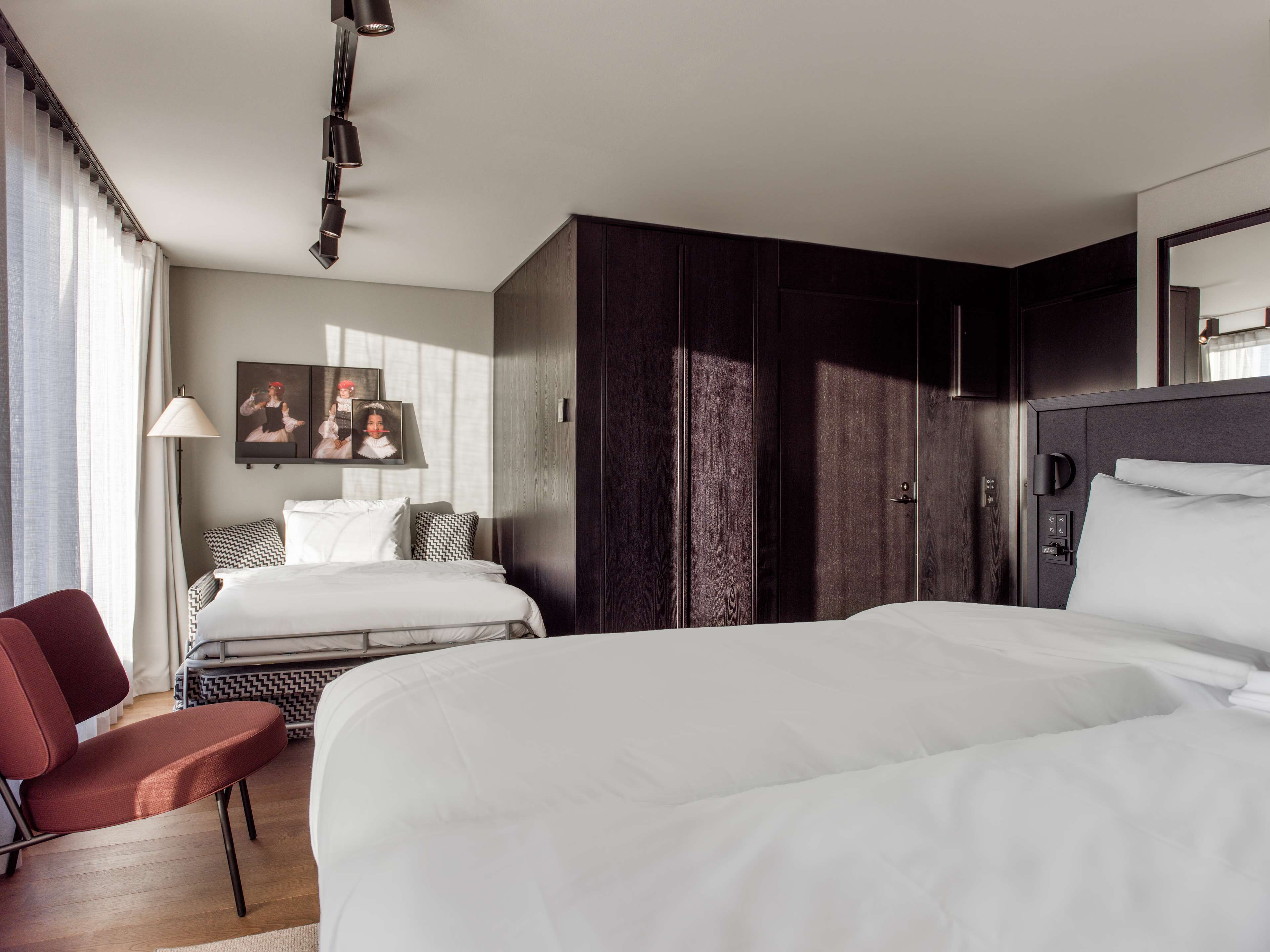 A hotel room with a large bed, a smaller bed, a desk with a chair, a wardrobe, and a mirror.