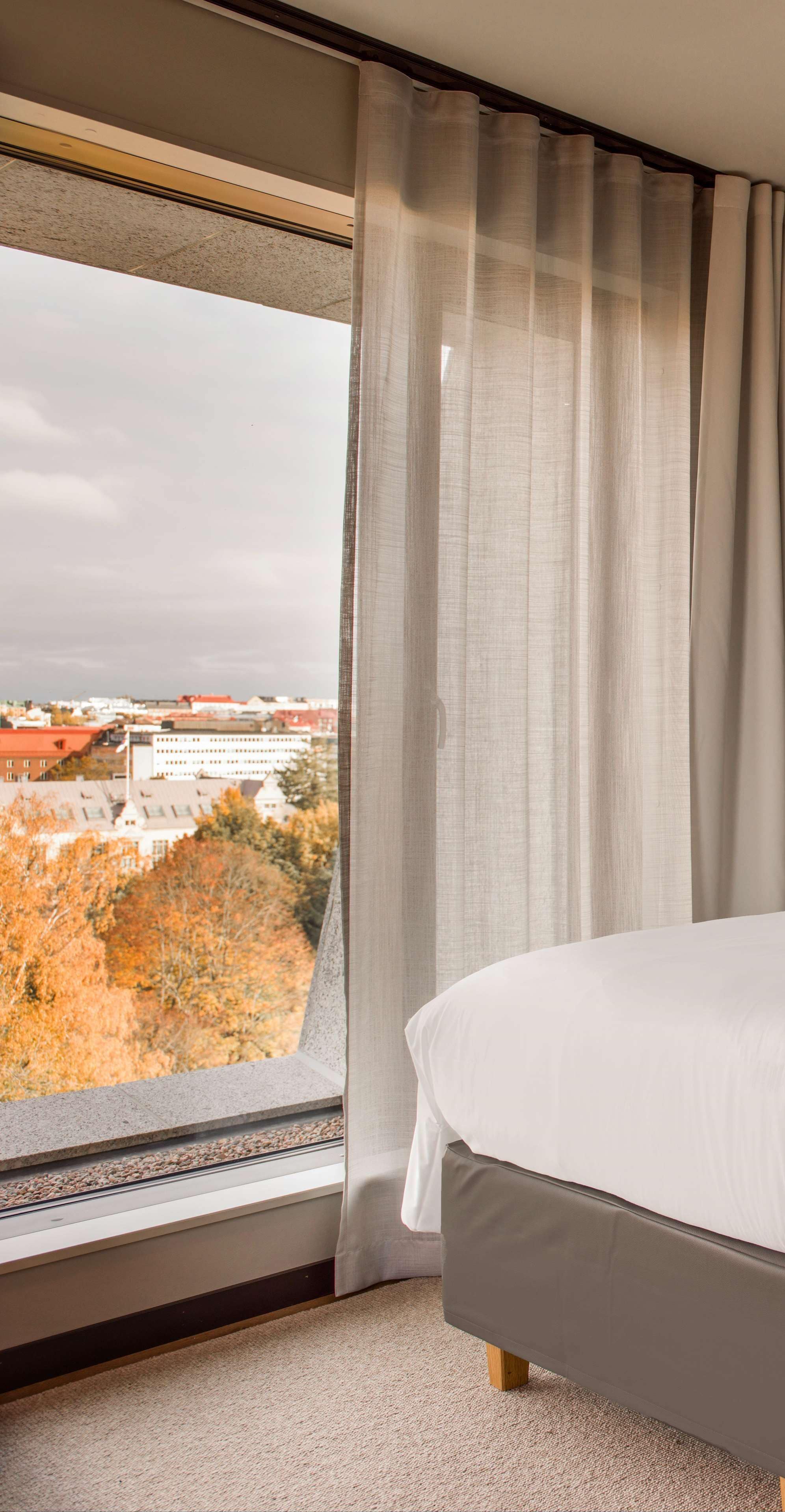 Hotellihuone, jossa on suuri ikkuna, sänky ja näkymä kaupungin ylle.