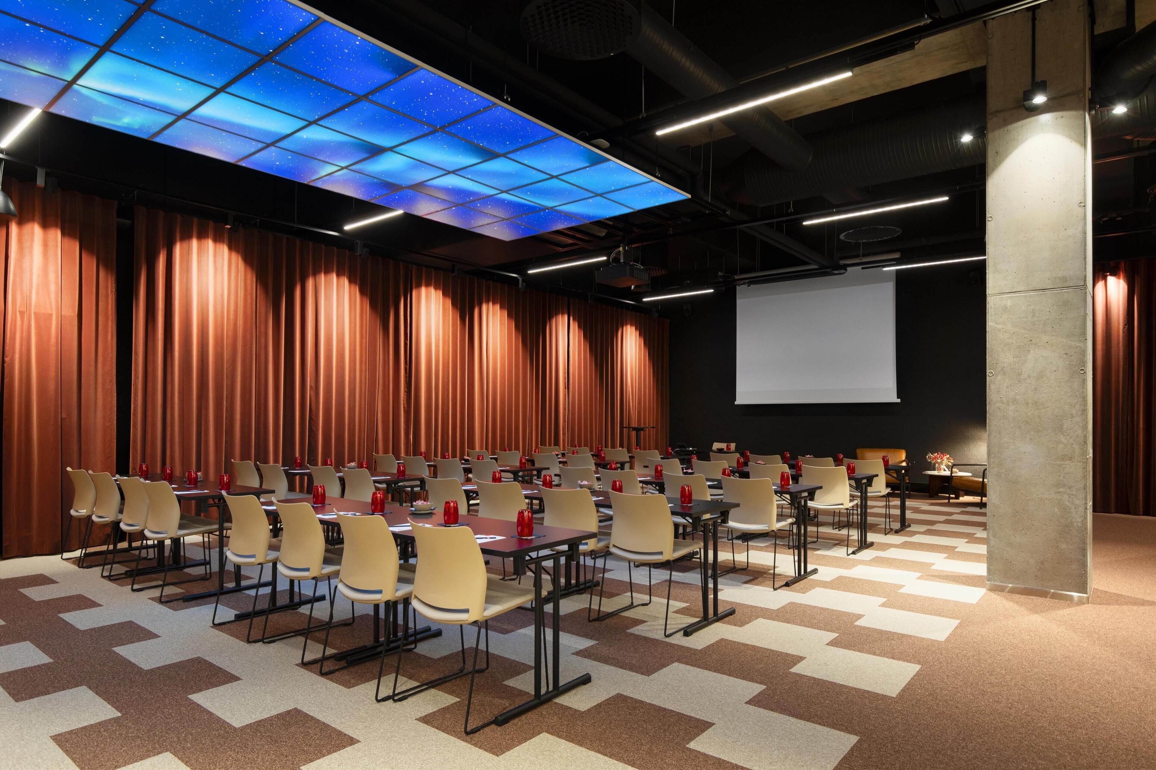 A conference room with a starry ceiling, rows of tables and chairs, and a projector screen.