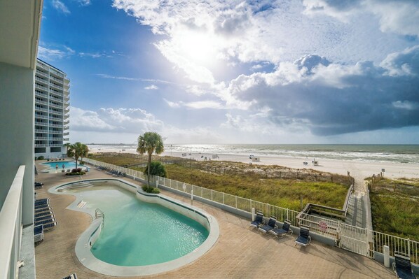 A pool area with a view of the beach, a palm tree, and a building in the background. - 3BD Condo @ The Lighthouse 215 (Gulf Shores)