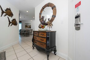 A hallway with a wooden cabinet, a mirror, and wall decorations including fish and a sun. - 3BD Condo @ The Lighthouse 215 (Gulf Shores)