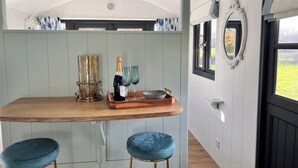 Un comedor con una mesa de madera, dos taburetes azules, una botella de champán y una bandeja con vasos.