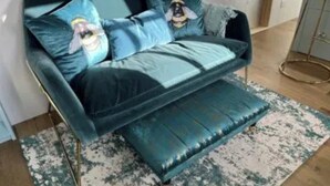 Un sofá tapizado en color verde azulado con cojines a juego y un reposapiés del mismo tono, sobre una alfombra estampada.