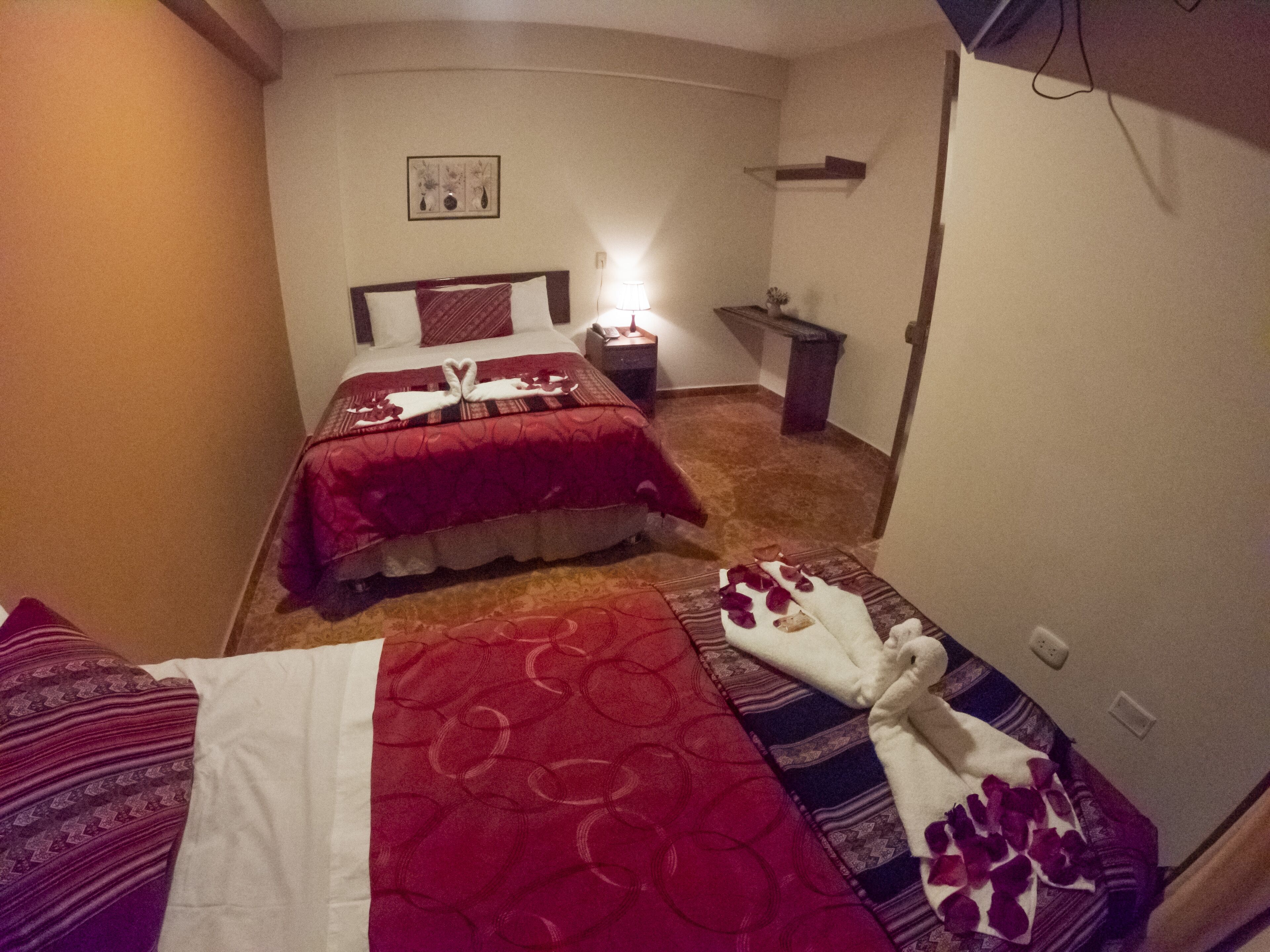 Une chambre d’hôtel avec deux lits, chacun recouvert d’une couverture rouge et doté d’un oreiller blanc. On y trouve une petite table avec une lampe, ainsi qu’un cadre photo accroché au mur.