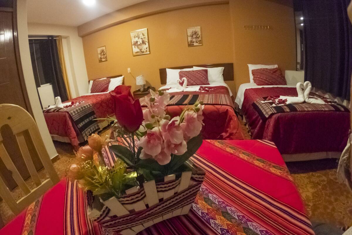 Une chambre d’hôtel avec trois lits, une table à manger ornée d’un vase de fleurs et une chaise.
