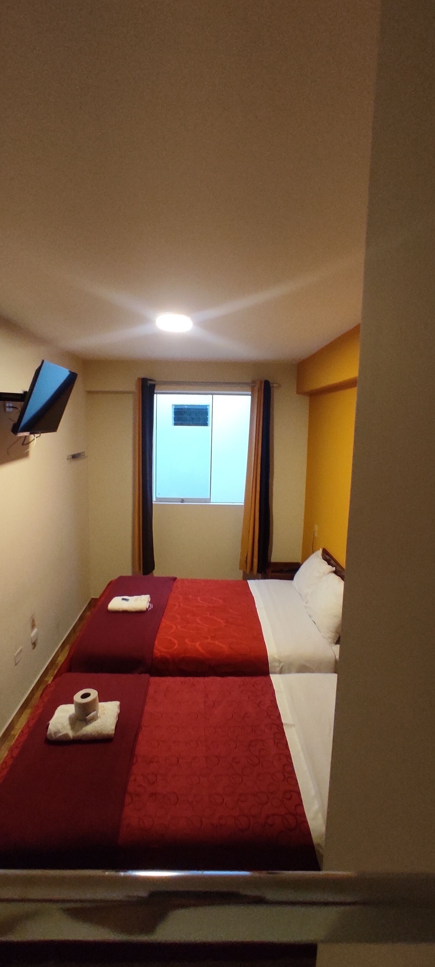Habitación de hotel con dos camas, un televisor de pantalla plana montado en la pared, una ventana con cortinas y un ventanal con vistas.