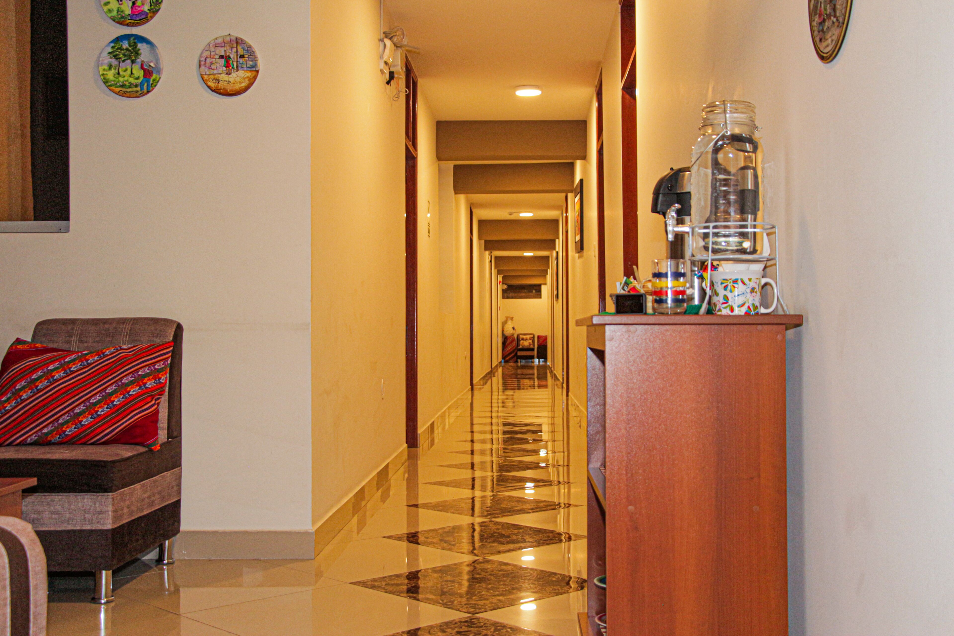 A hotel hallway with a polished floor, a sofa with a patterned cushion, and a coffee station with a water dispenser.
