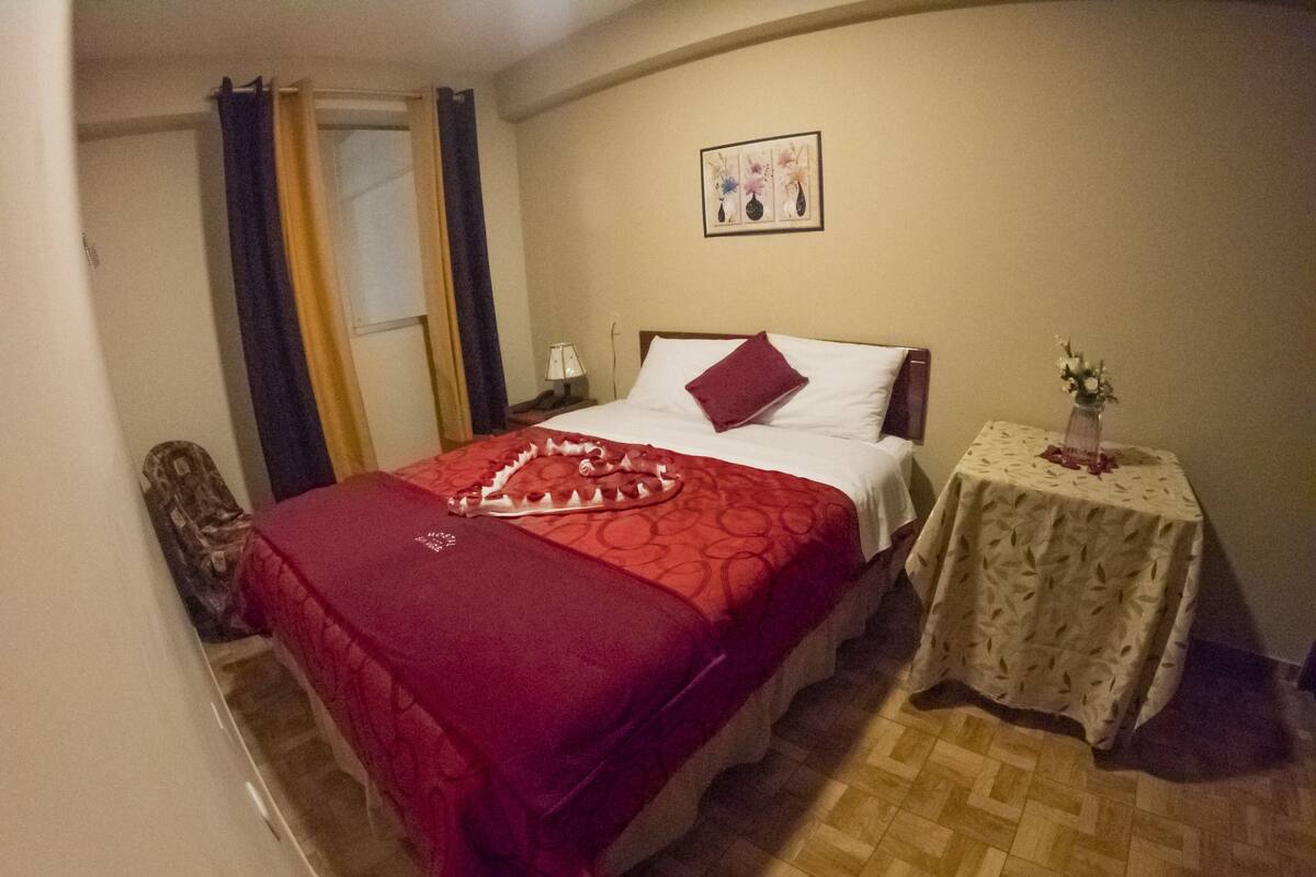 Une chambre d’hôtel avec un lit, une table de chevet, une petite table avec un vase et une porte avec des rideaux.