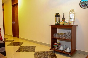 A hotel lobby with a wooden reception desk, a coffee machine, a bottle, and a glass jar on the counter.