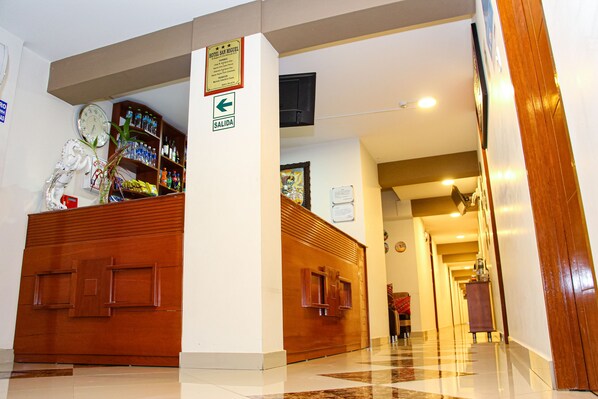 A hotel lobby with a reception desk, a clock, and a sign indicating the exit.