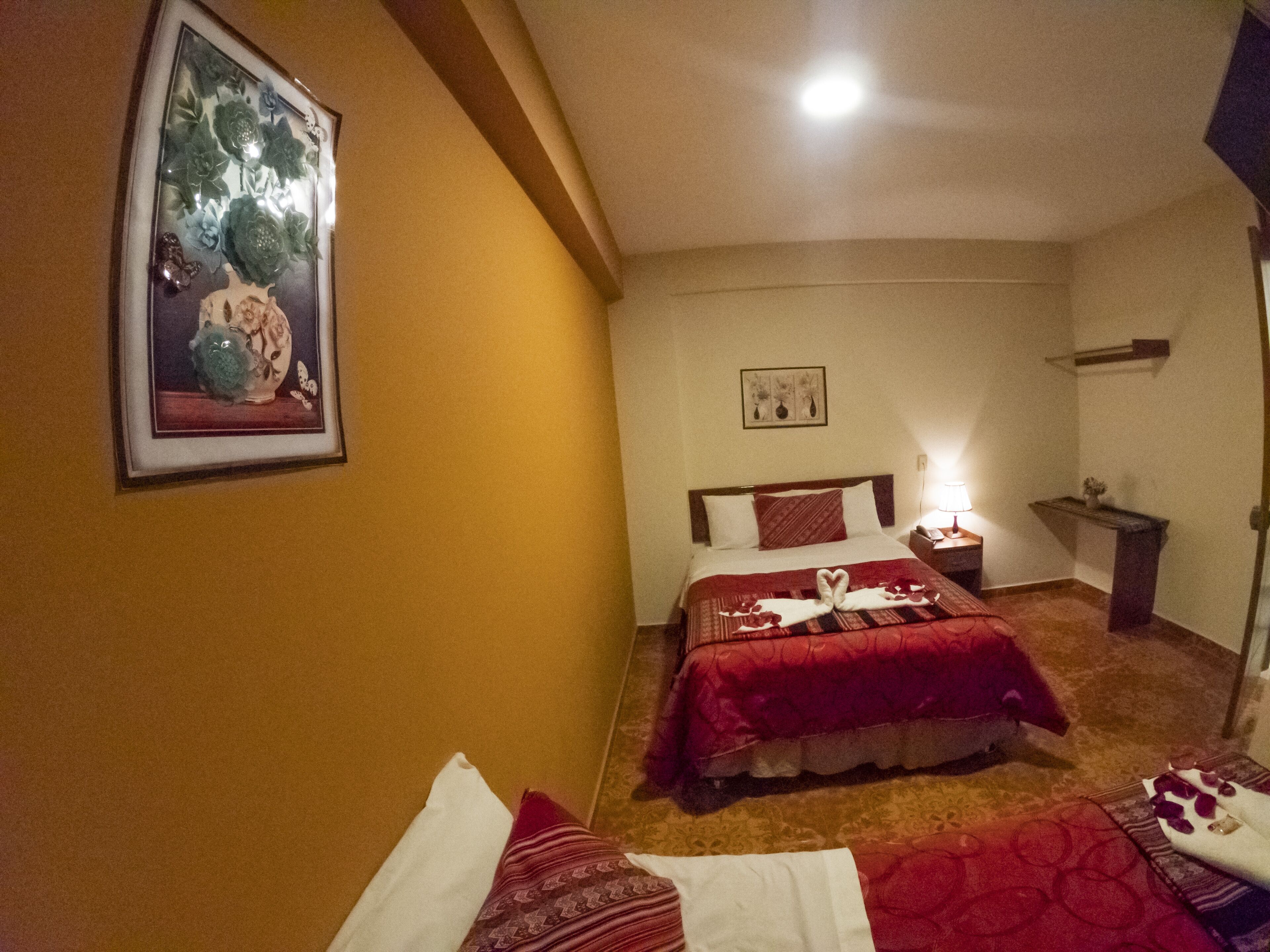 Ein Hotelzimmer mit Bett, Nachttisch, einem gerahmten Bild an der Wand und einem kleinen Tisch mit Lampe.
