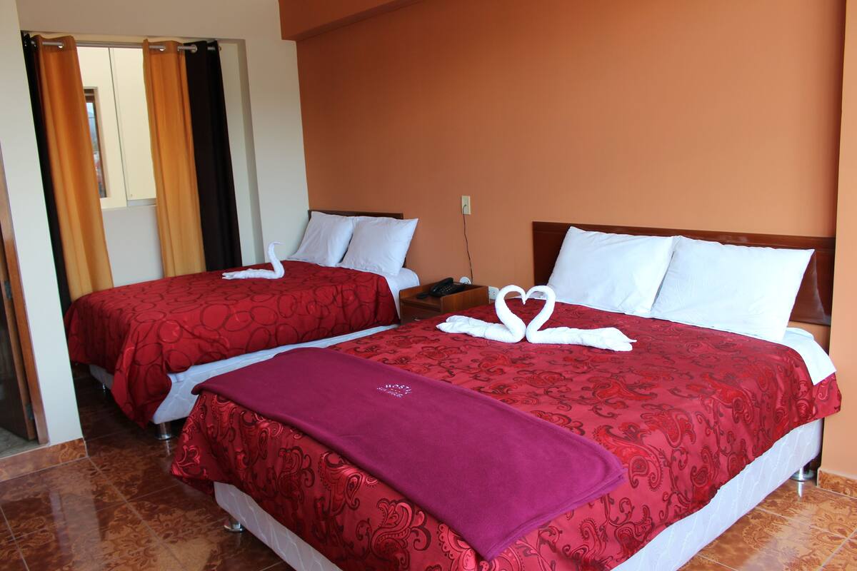 Une chambre d’hôtel avec deux lits, chacun recouvert d’une literie rouge et orné d’oreillers blancs, et une couverture rouge jetée sur le lit situé au premier plan.