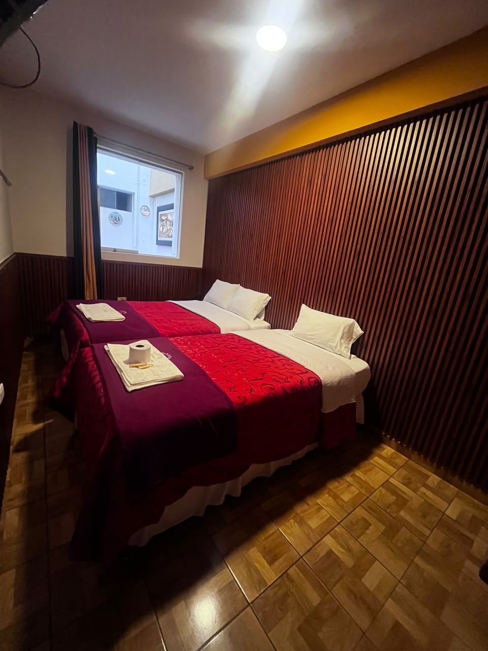 Habitación de hotel con dos camas, piso de madera y ventana con cortinas.