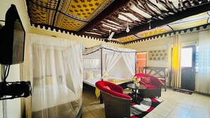 A room with a bed under a canopy, a television, a red chair, and a small table with a vase.