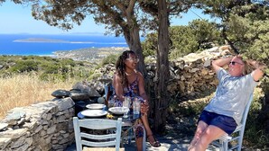 Two people seated at a table outdoors with a stone wall and a tree in the background. - Cosy open plan studio for couples or singles (Alyki)