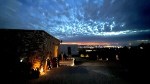 A stone building with a paved area and lights, a clear sky with clouds, and a distant cityscape at dusk. - Cosy open plan studio for couples or singles (Alyki)