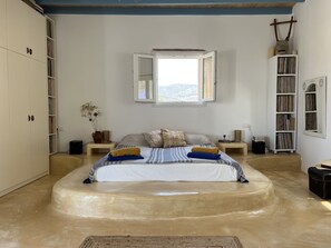 A bedroom with a large bed, a window with an open view, a bookshelf, and a wardrobe. - Cosy open plan studio for couples or singles (Alyki)
