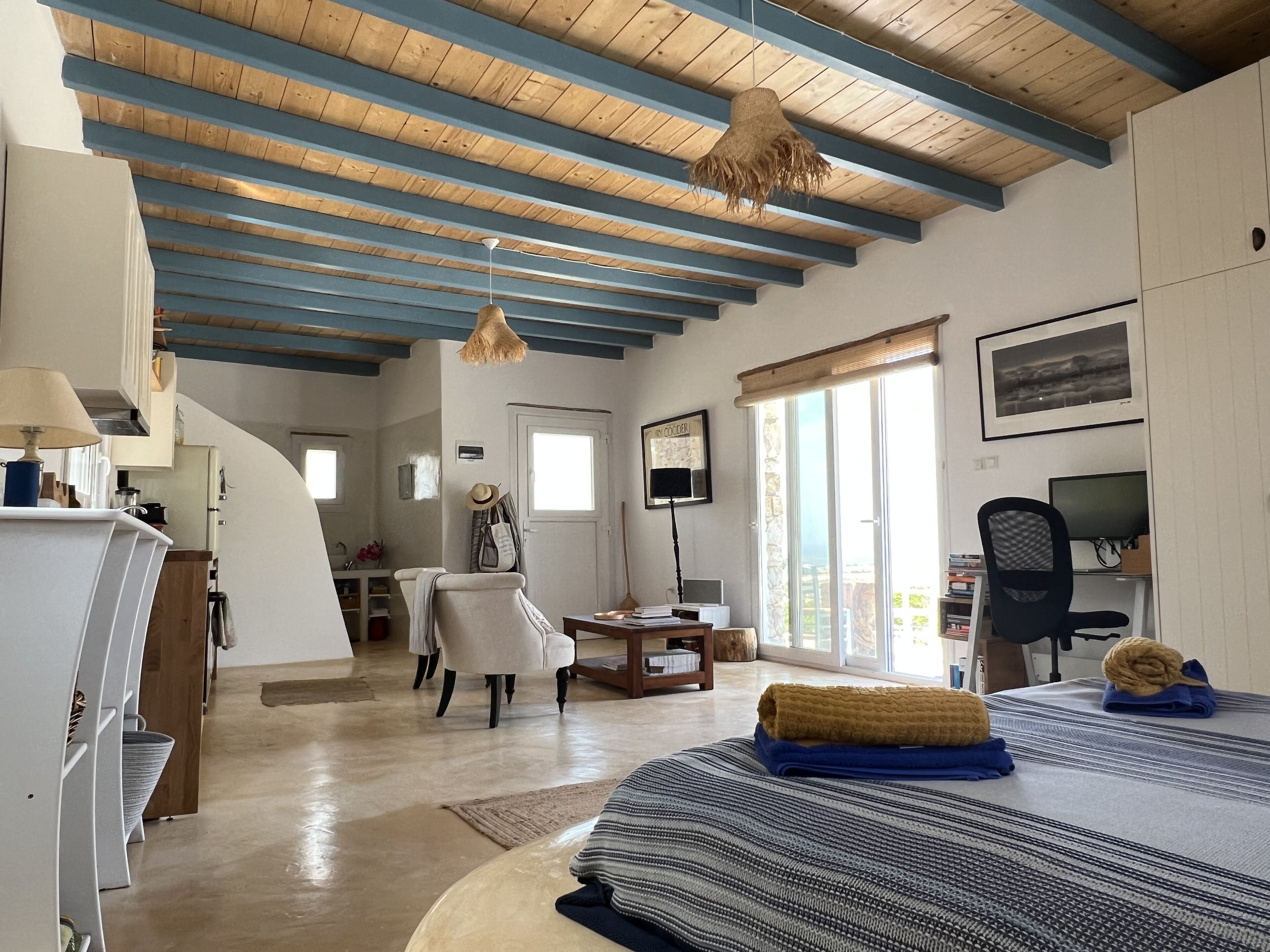 Une pièce spacieuse avec un plafond haut, un lit recouvert d’une couverture à rayures, un bureau avec un ordinateur et une chaise.