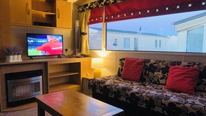 A living room with a television, sofa, and a window with curtains. - Sleeps 6, Gym, Entertainment, Pool, Beach (Rhyl)