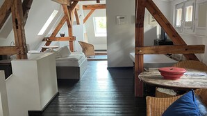 An attic bedroom with exposed wooden beams, a sloped ceiling, a bed, a wicker chair, and a small table. - Park Residenz Bei Wu (Wesenberg)