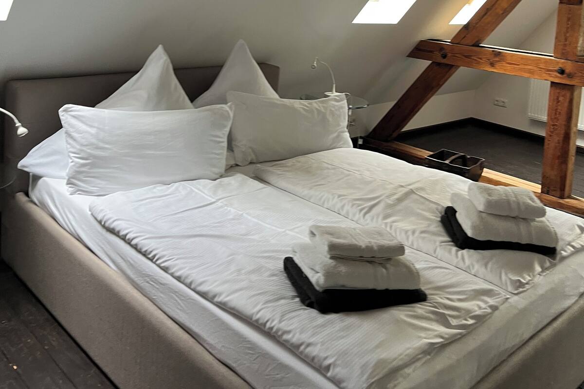 A bedroom with a sloped ceiling, a bed with white linens, and a skylight.