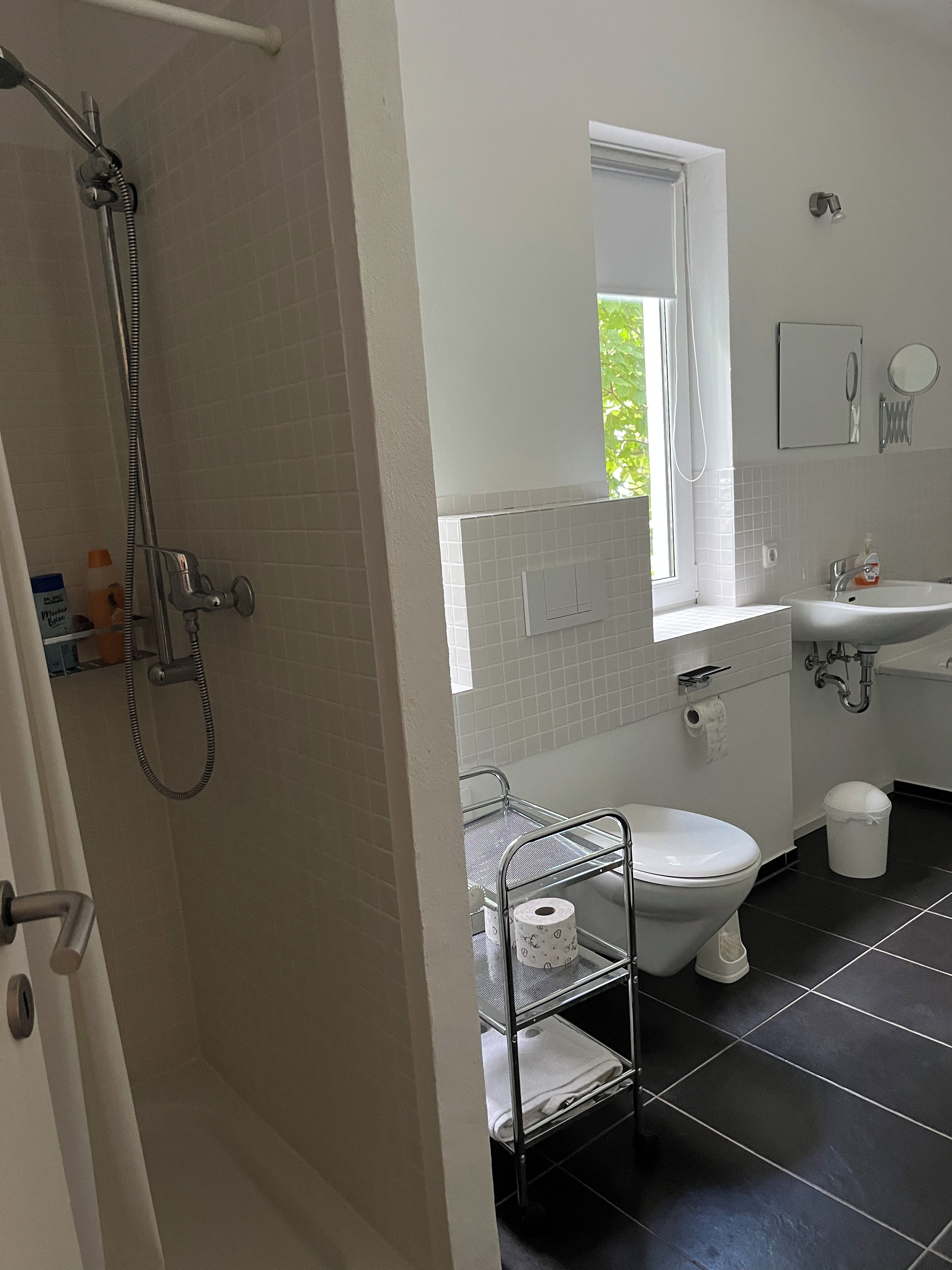 A bathroom with a shower, toilet, sink, and a window.