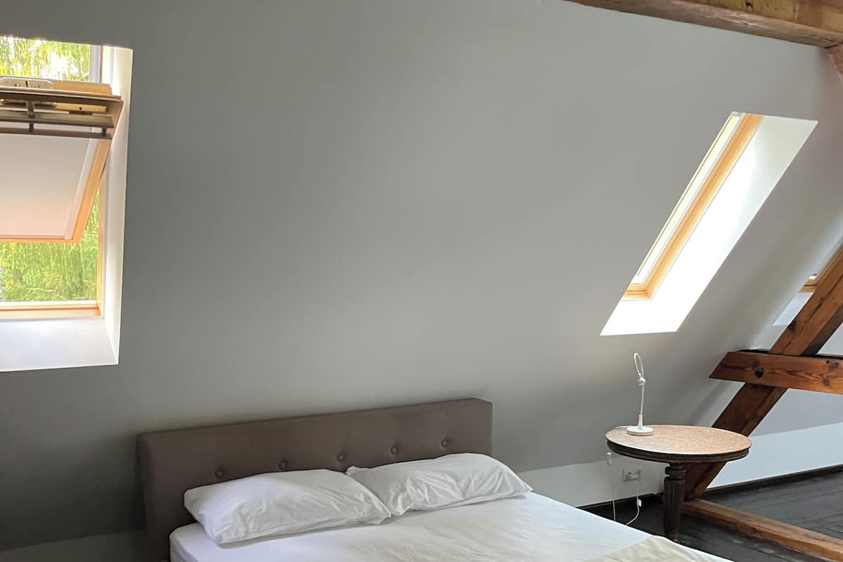 Une chambre Ă coucher avec un lit, une lucarne et une petite table.