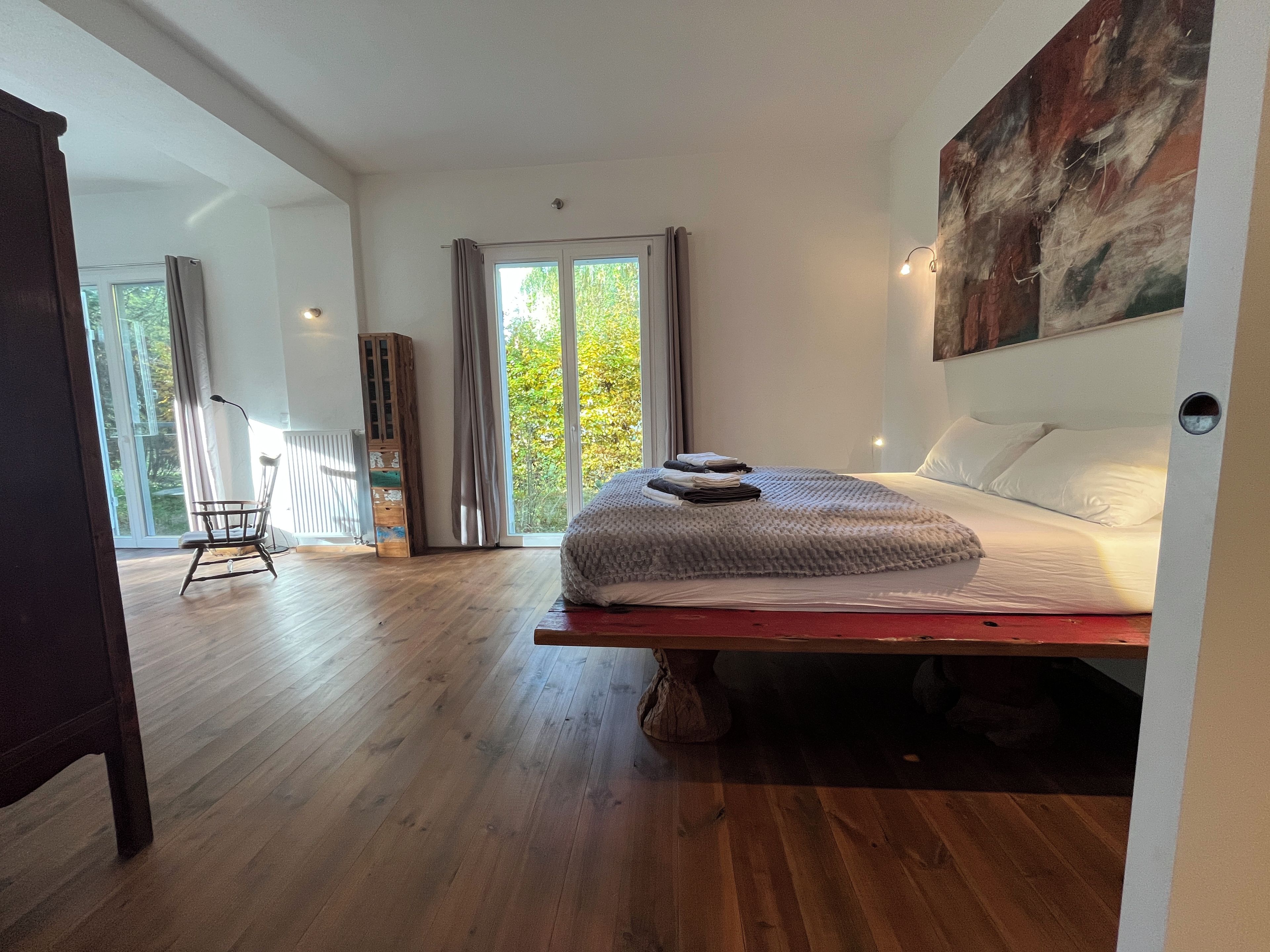 Un dormitorio con una cama, una silla, una ventana y un cuadro en la pared.