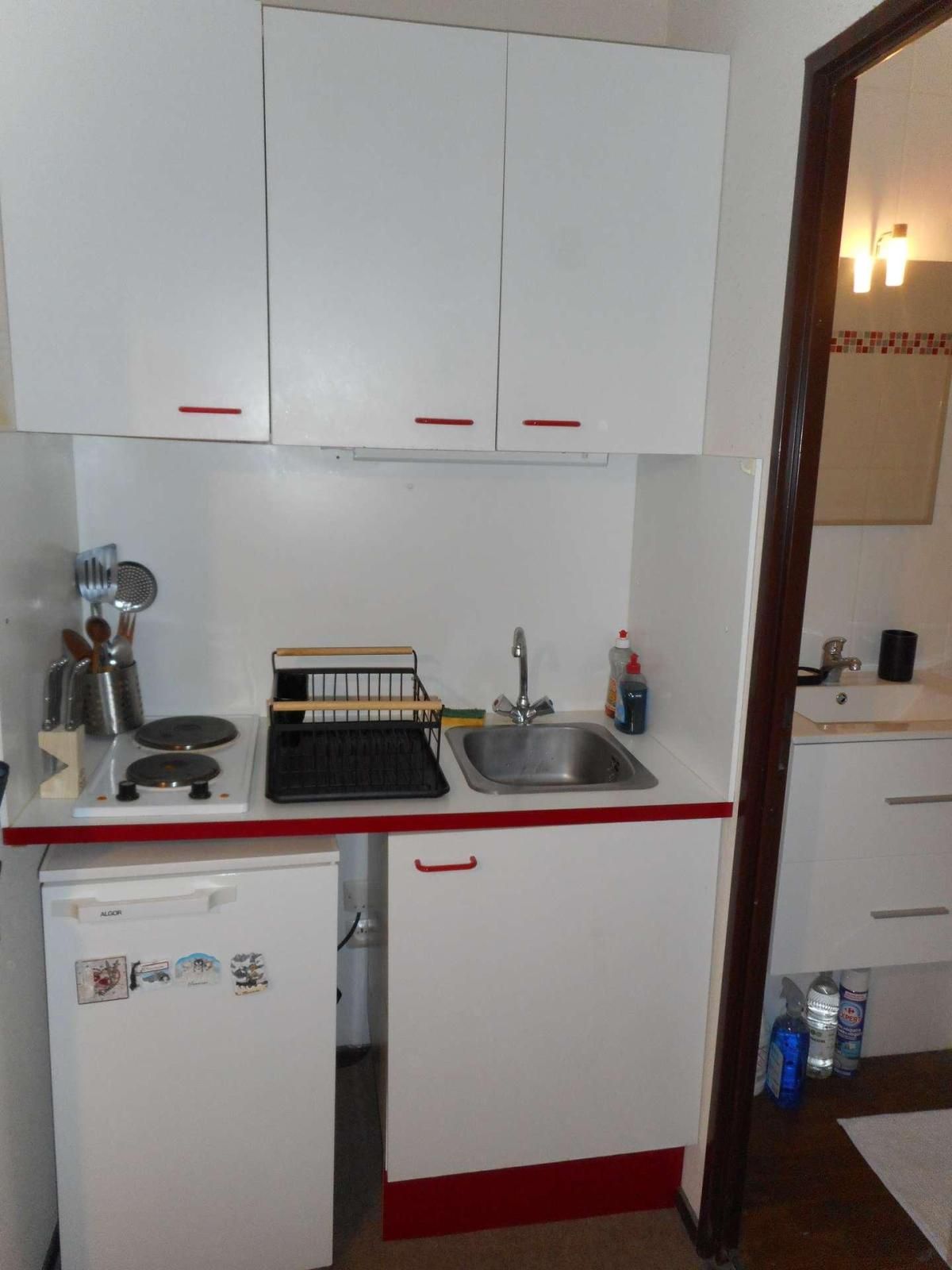 Eine kleine Küche mit weißen Schränken, einem Kühlschrank, einer Spüle und Grundausstattung.