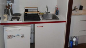 Une cuisine de taille réduite, avec des meubles blancs, un petit réfrigérateur, un évier et les ustensiles de base.