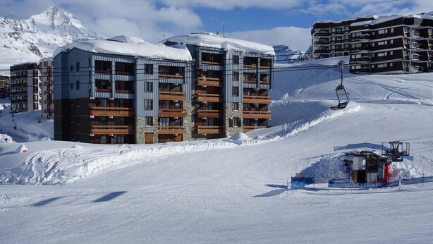 A multi-story hotel with balconies, a ski lift, and a snowy mountain backdrop.