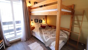 A bunk bed room with a wooden ladder, a white rug, and a window with curtains.