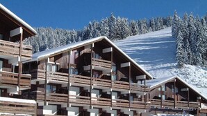 Ein Chalet mit mehreren Balkonen und einer Skipiste im Hintergrund.