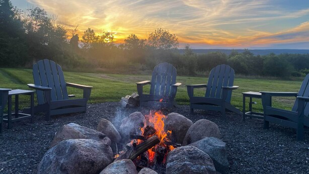 A fire pit with four Adirondack chairs around it, set on a gravel surface with a sunset view in the background. - Spacious Hammondsport Home on 6 Acres w/ Lake View (Hammondsport)