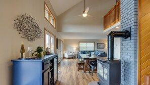 A modern living room with a fireplace, a dining area, and a kitchen with a blue island. - Spacious Hammondsport Home on 6 Acres w/ Lake View (Hammondsport)