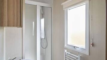 Een badkamer met een douche, een wastafel en een raam.