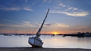 Ein Segelboot liegt vor einem Kiesstrand vor dem Hintergrund eines Sonnenuntergangs.